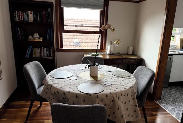 Un comedor con una mesa redonda, dos sillas, una estantería, una ventana y una lámpara.