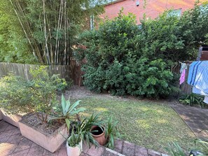 A garden with various plants, a wooden fence, and a brick wall in the background. - Cosy 2-bed comfy art deco home away from home (Cammeray)