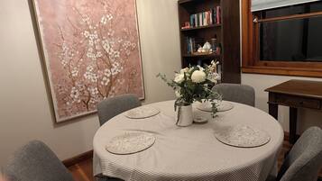A dining area with a round table, grey chairs, a bookshelf, and a large floral painting.