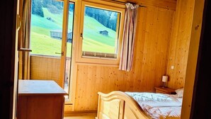 Une pièce en bois, avec un lit, un bureau et une fenêtre donnant sur un paysage verdoyant.