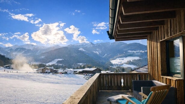 Une terrasse en bois offrant une vue sur des montagnes enneigées et une piste de ski.