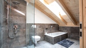 Une salle de bain moderne avec une douche à parois de verre, des toilettes blanches, une baignoire sur pieds et un plafond en bois.