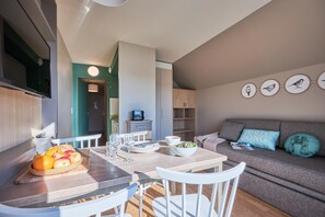 A modern kitchen with a dining table, chairs, and a fruit basket. - Courseulles Coastal Apartment for 4 (Courseulles-sur-Mer)