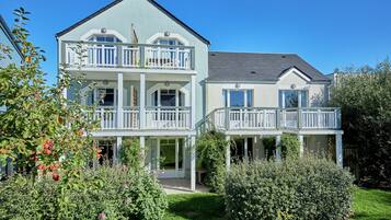 A two-story house with a balcony, surrounded by greenery and a well-maintained lawn.