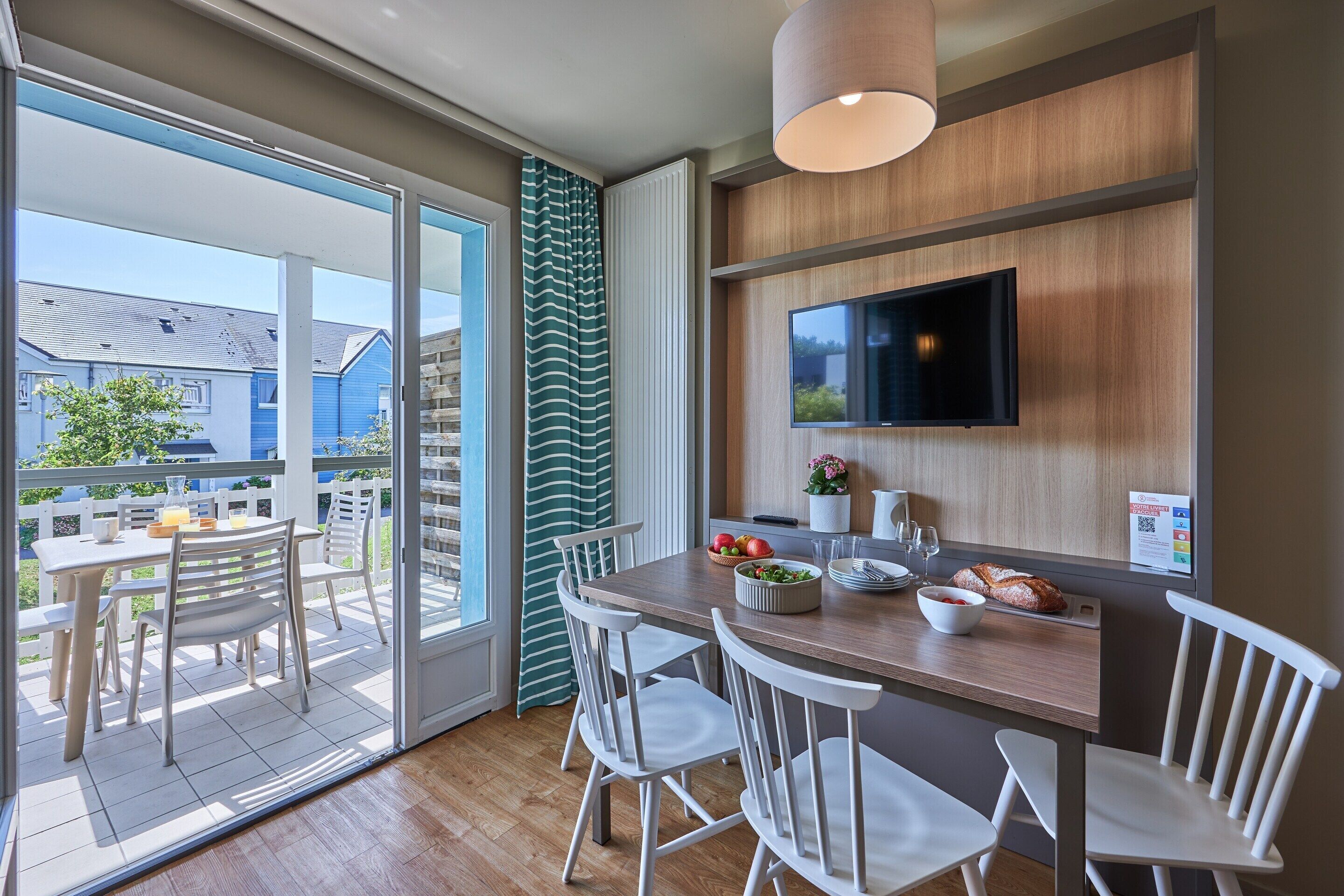 Une cuisine moderne avec un plan de travail en bois, des chaises blanches et un téléviseur fixé au mur.