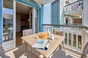 A balcony with a table set for breakfast, a magazine, and a wooden bowl with fruit. - Courseulles Coastal Apartment for 4 (Courseulles-sur-Mer)
