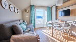 Uma sala de estar moderna com sofá, mesa de jantar com cadeiras, televisão de tela plana e varanda com cortinas.