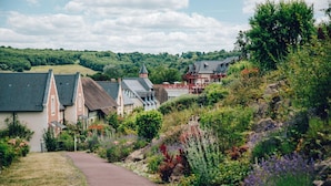 A pathway leading to traditional houses with steep roofs, surrounded by lush greenery and flowering plants. - Premium Normandy Apartment for 4 (Houlgate)