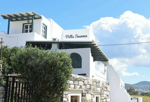 Ein weißes Gebäude mit der Aufschrift 'Villa Joanna' auf der Fassade, Steinmauern und blauem Himmel.