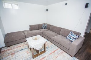 Ein Wohnzimmer mit einem Ecksofa, einem kleinen Tisch und einem gemusterten Teppich.