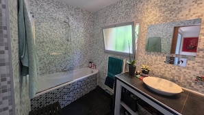 Un bagno con vasca, lavandino, finestra e specchio.