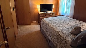 Ein Hotelzimmer mit Bett, Fernseher auf einem Schminktisch, einer Tür und einem Fenster mit Vorhängen.