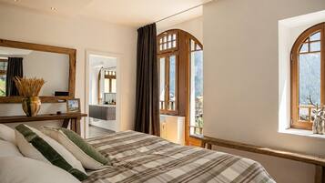A bedroom with a large bed, a mirror, a window with curtains, and a view of the outdoors.