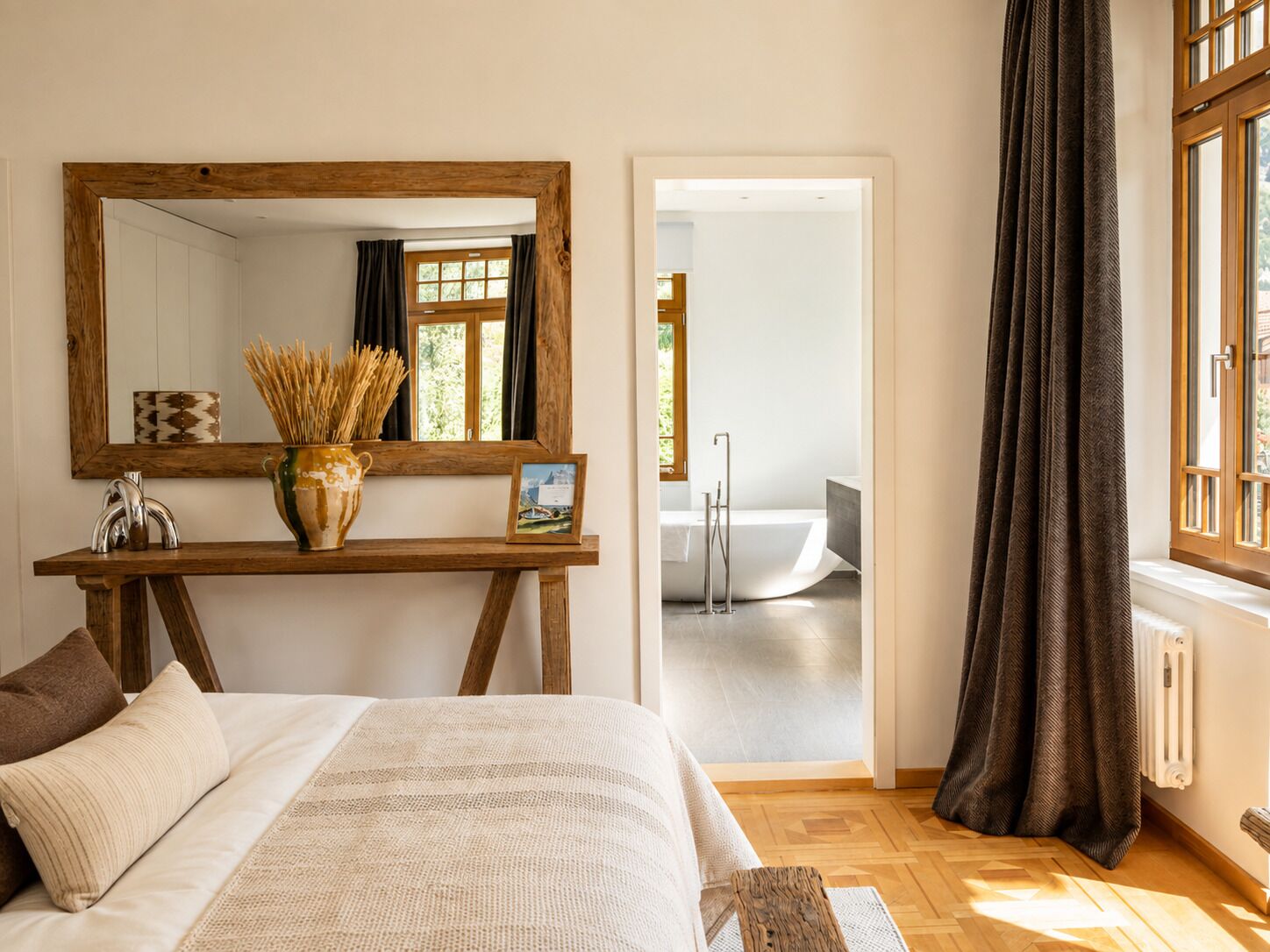 A bedroom with a large bed, a wooden bedside table, a mirror, and a view into the bathroom.