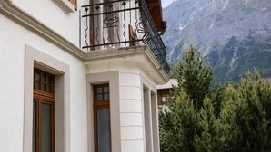 Un edificio con un balcone, un sentiero in pietra e montagne sullo sfondo.