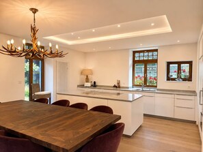 Une cuisine moderne avec un Ăźlot central, un coin repas avec une table et des chaises en bois, et un lustre.