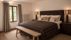 Una camera da letto con un letto, una panca, comodini e una finestra con tende.