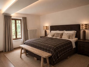 Une chambre Ă coucher avec un lit, une banquette, des tables de chevet et une fenĂȘtre avec des rideaux.