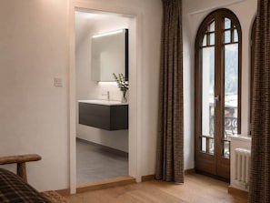 Une piĂšce dotĂ©e dâun plancher en bois, dâune salle de bain moderne avec un miroir et un lavabo, et offrant une vue par une fenĂȘtre agrĂ©mentĂ©e de rideaux.