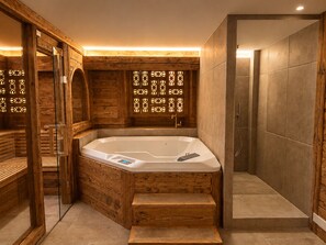 A wooden cabin-style bathroom with a freestanding bathtub, a shower area, and a glass-enclosed sauna.