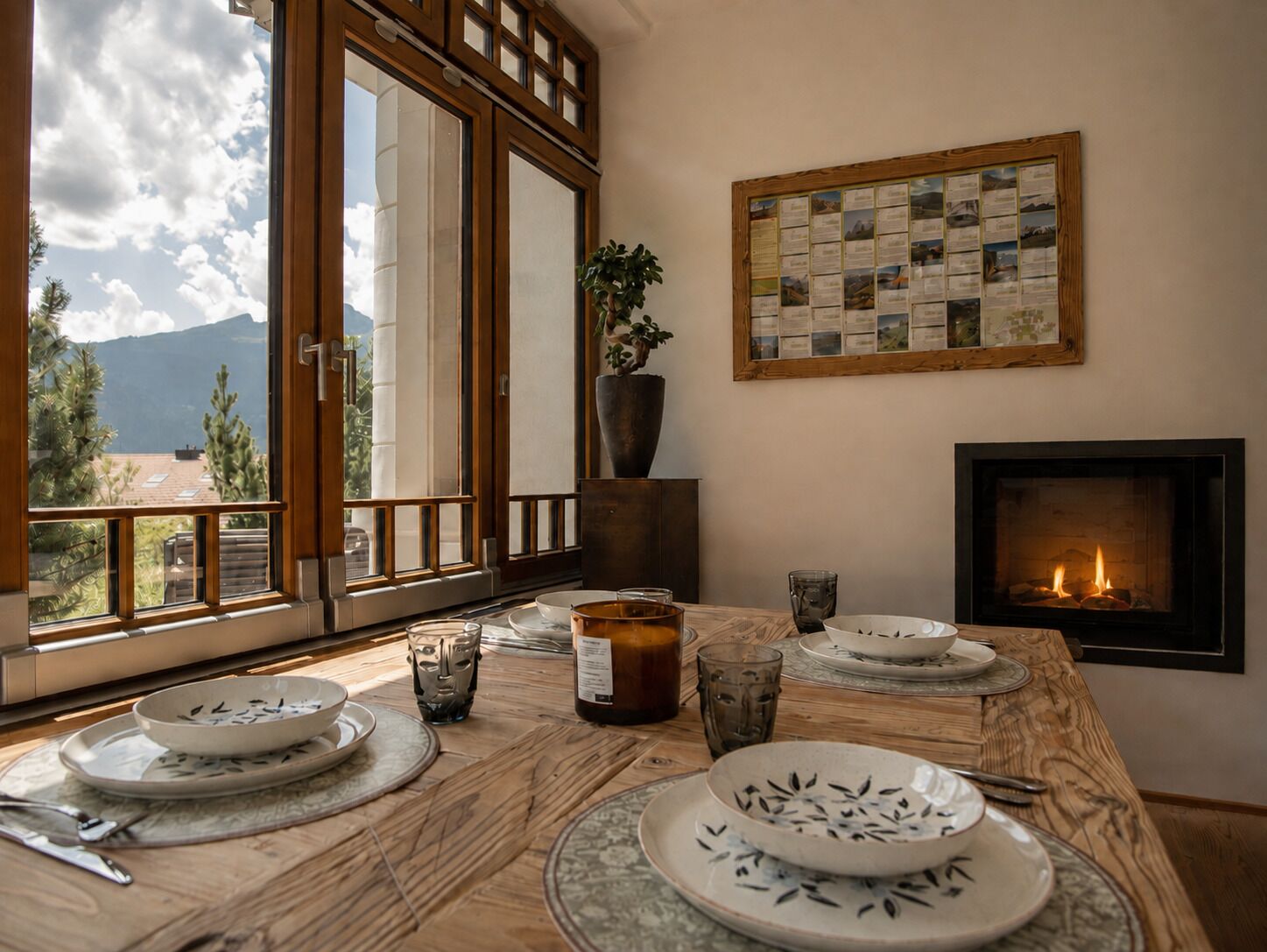 Un coin repas avec une table dressée pour quatre personnes, une cheminée et une vue sur les montagnes par une grande fenêtre.