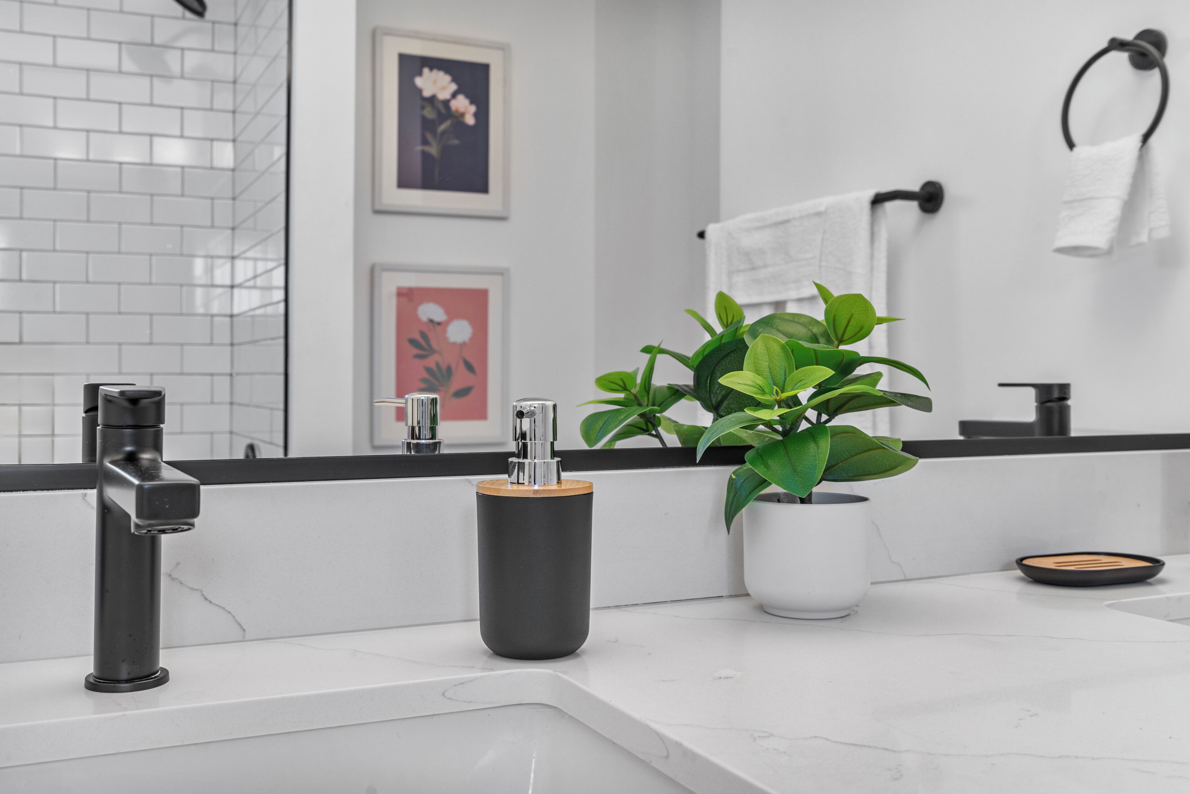 A modern bathroom with a white sink, black faucet, and a potted plant.