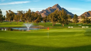 Un campo da golf con uno stagno, alberi e montagne sullo sfondo.