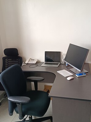 Una taula amb un ordinador portàtil, un monitor, un teclat, un ratolí i una cadira.