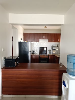 A kitchen with wooden cabinets, a black refrigerator, a stove, and a water dispenser. - Fantastic 2-bedroom apartment in tranquil Pridelands with AC (Pridelands)