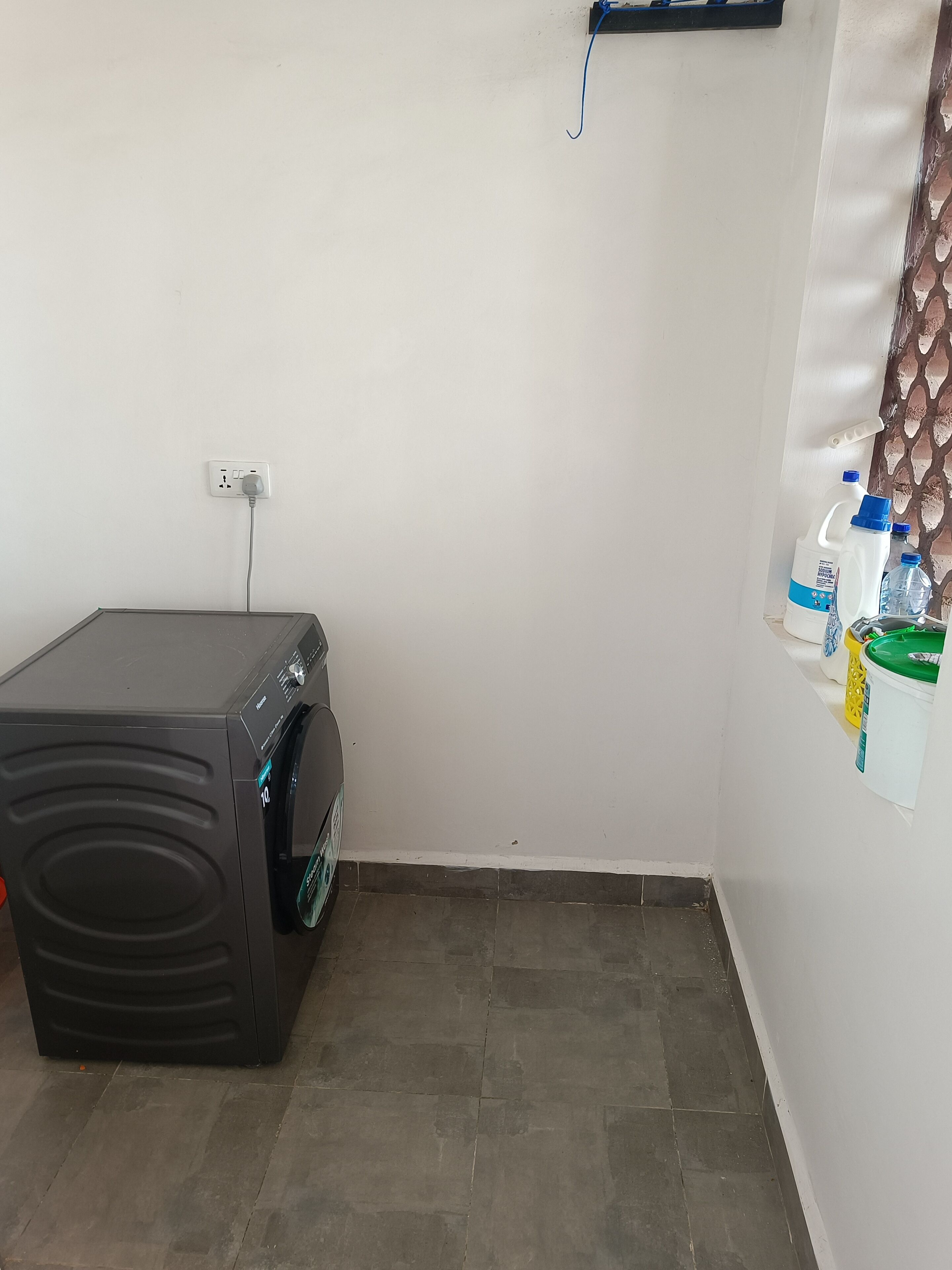 Una sala de lavandería con lavadora, toma corriente y productos de limpieza en la pared.