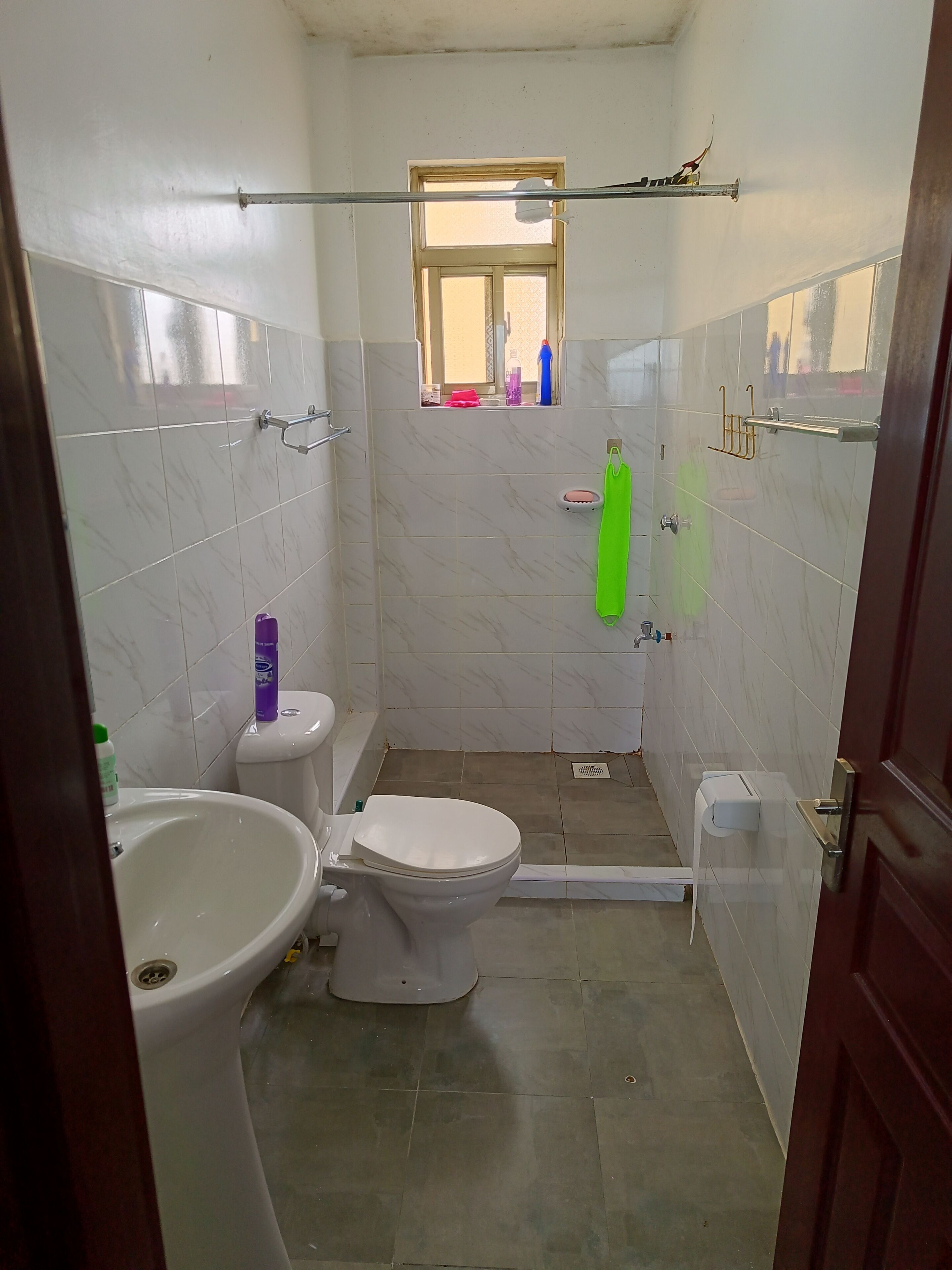 Et lille badeværelse med toilet, bidet og håndvask. Der er et vindue over toilettet og en håndklæderække på væggen.