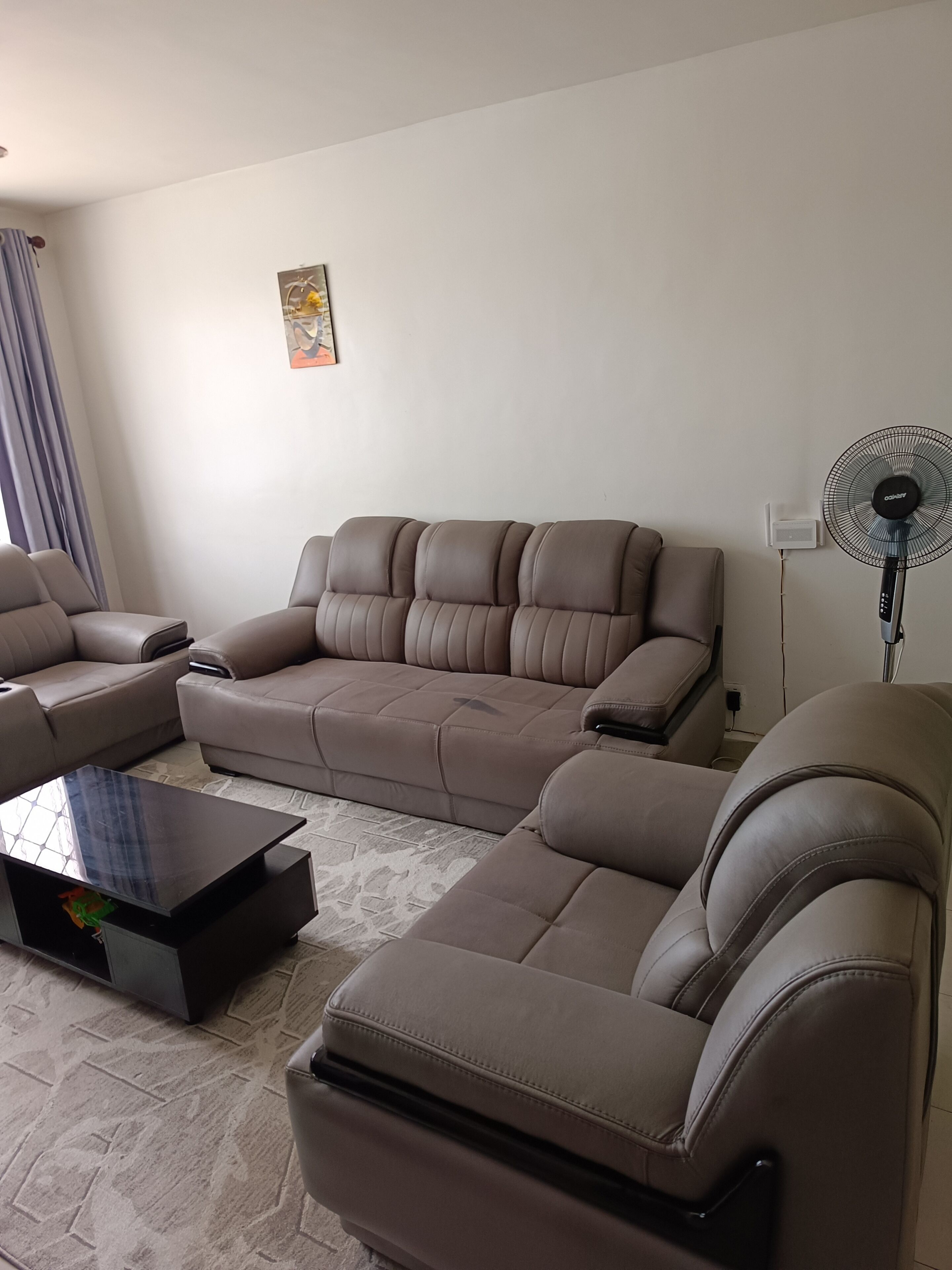 A modern living room with a sectional sofa, a coffee table, and a standing fan.