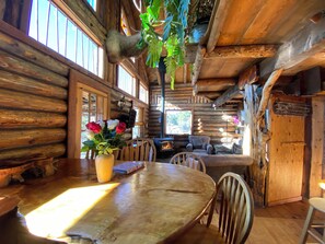 Ein rustikales Blockhaus-Interieur mit Holzesstisch, Stühlen, einer Couch und einem Kamin.
