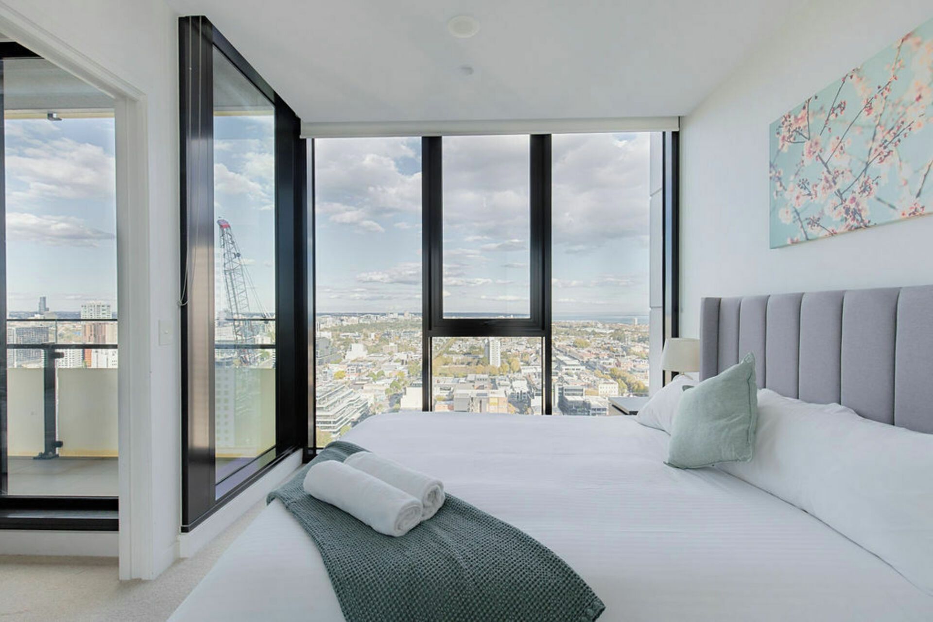 A modern bedroom with a large bed, a view of the cityscape, and a balcony with a glass door.