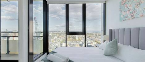A modern bedroom with a large bed, a view of the cityscape, and a balcony with a glass door.