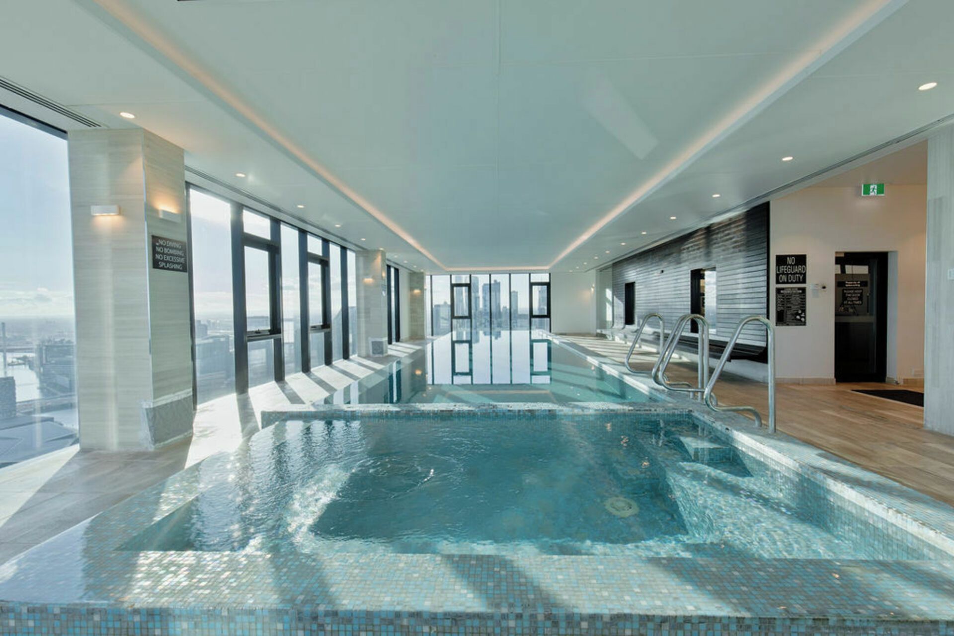 Une piscine intérieure moderne avec des parois en verre transparent, un sol carrelé et une vue sur la ville.