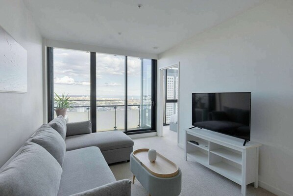 Ein modernes Wohnzimmer mit großem Fernseher, grauem Sofa und einem Balkon mit Blick.