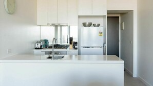Une cuisine moderne avec des meubles blancs, un réfrigérateur en acier inoxydable et un four encastré.