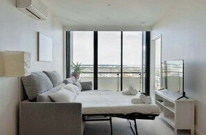 A modern bedroom with a bed, a sofa, a TV, and a large window with a city view. - Executive 2BDR in Southbank w Parking. (Southbank)