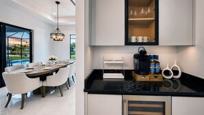 A modern kitchen with a black marble countertop, a coffee maker, and a cabinet above the counter. -  Luxury Waterfront Villa : Pool, Jacuzzi, Outdoor TV & Theater (Cape Coral)