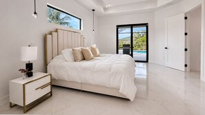 A modern bedroom with a large bed, a bedside table, a lamp, and a view of the outdoors. -  Luxury Waterfront Villa : Pool, Jacuzzi, Outdoor TV & Theater (Cape Coral)