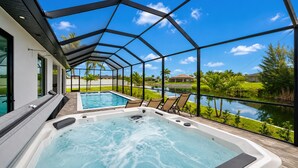 Un jacuzzi con vistas a una piscina y un lago, rodeado de sillas y un área cubierta.