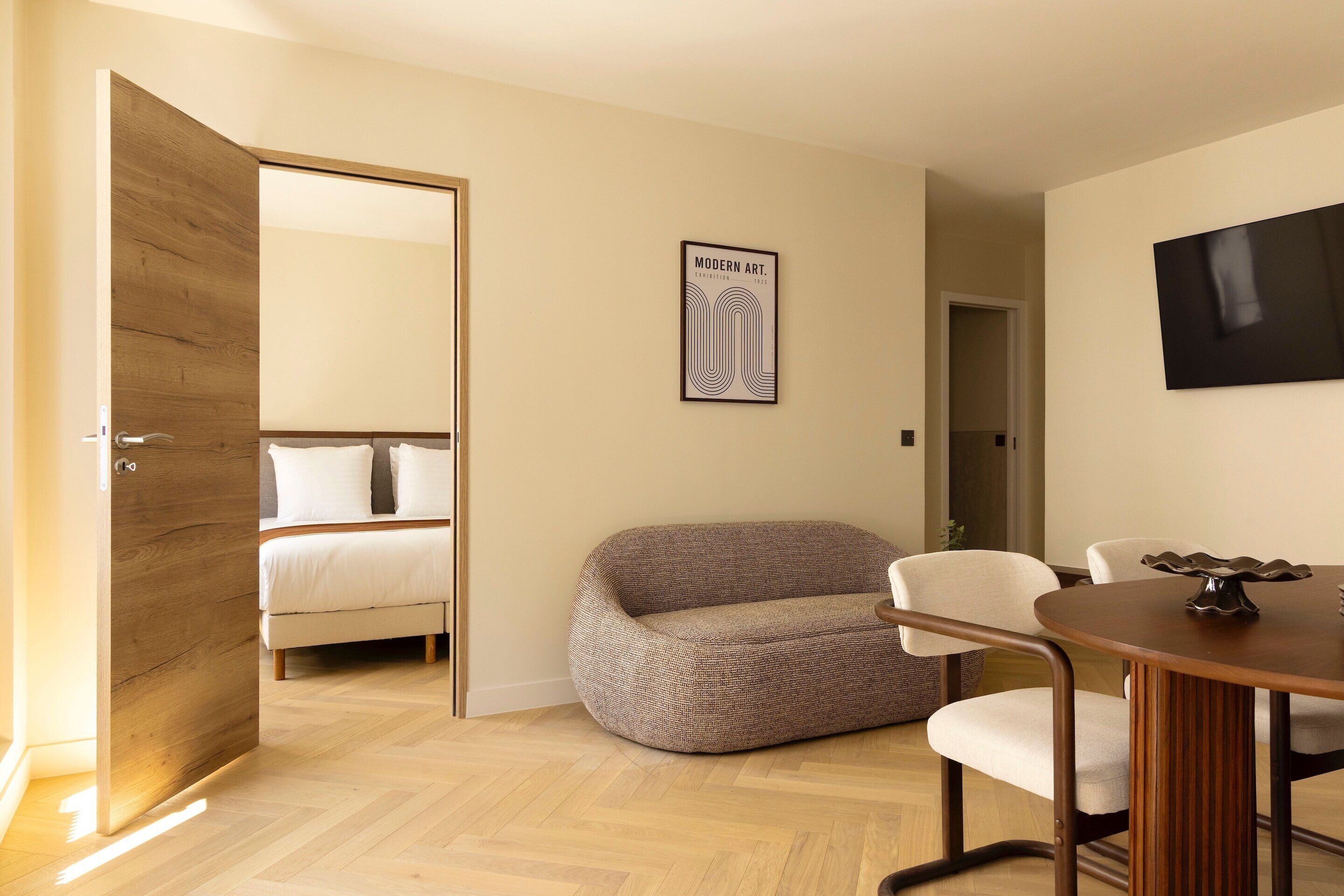 A modern room with a bed, a sofa, a dining table, and a TV on the wall.