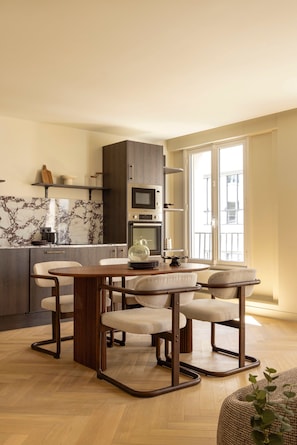 Eine moderne Küche mit Marmorfliesenspiegel, Holzschränken und einem Essbereich mit rundem Tisch und Stühlen.