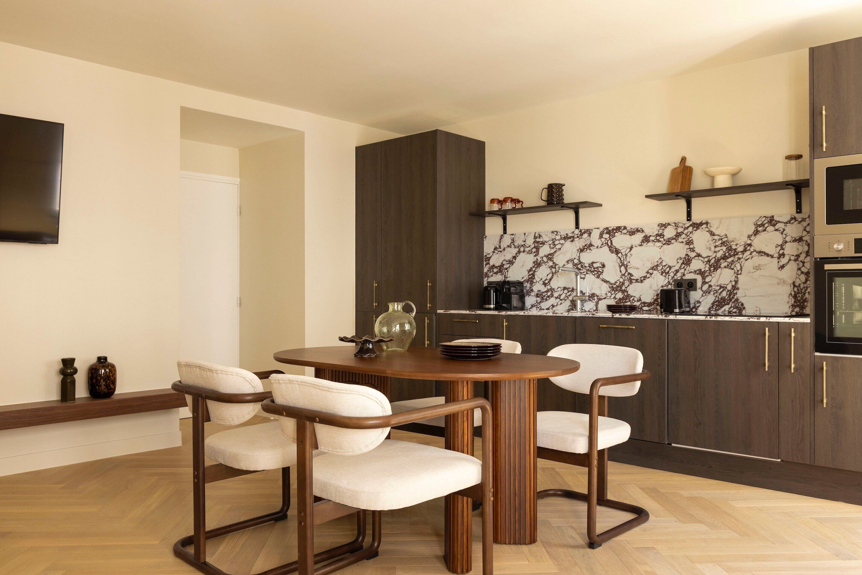 A modern kitchen with dark wood cabinets, a marble backsplash, and a dining area with a wooden table and four chairs.