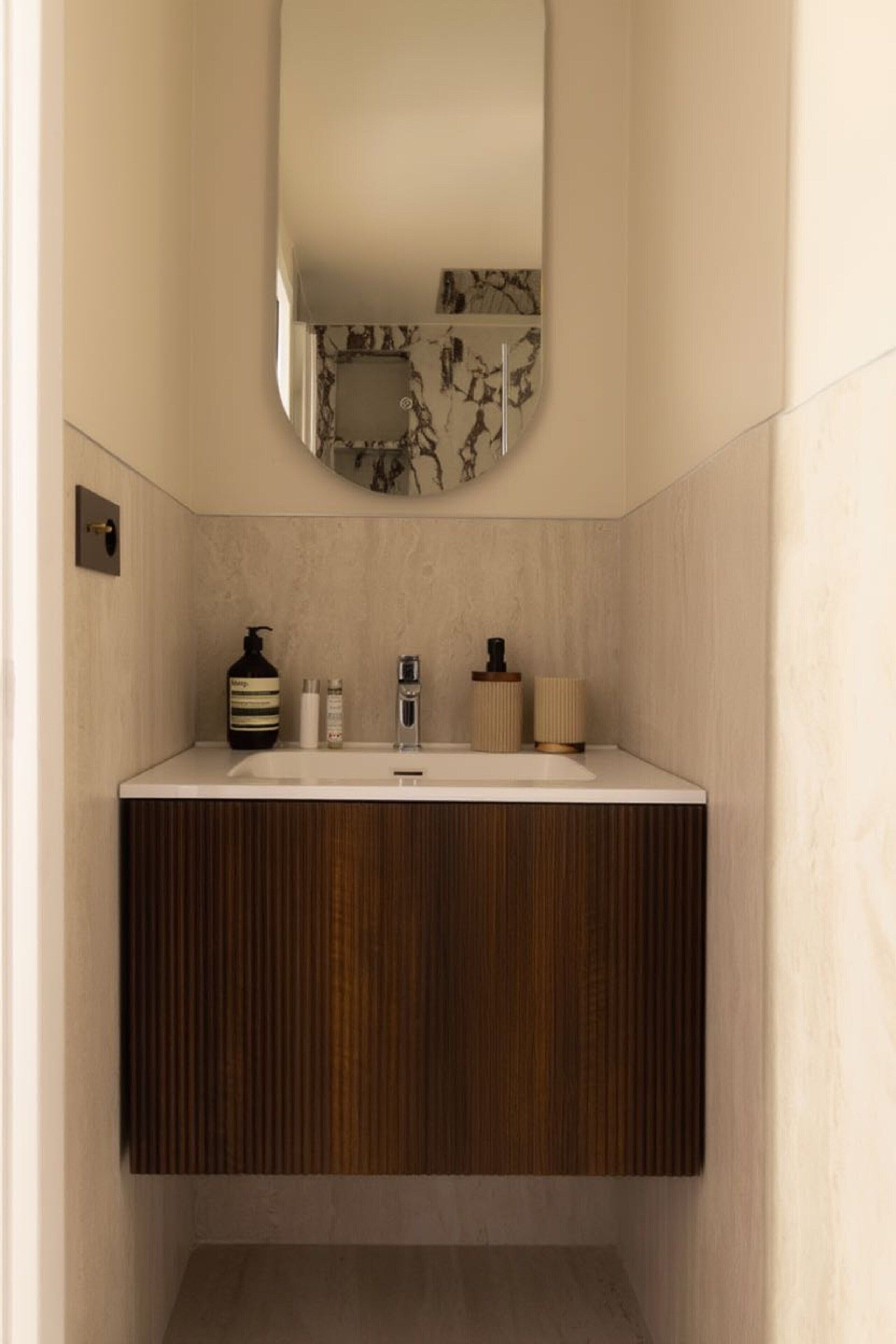 A modern bathroom with a marble backsplash, a wooden vanity, and a mirror.