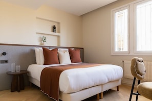Ein Schlafzimmer mit einem Bett, Nachttischen, einem Sessel, einem Heizkörper und einem Fenster.