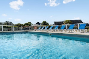 Ein Schwimmbecken mit blauem Wasser, umgeben von weißen Liegestühlen und einem weißen Zaun.