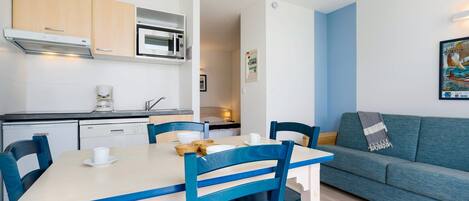 Une cuisine compacte équipée d’un four à micro-ondes, d’un four traditionnel et d’un lave-vaisselle. On y trouve une table à manger avec des chaises, ainsi qu’un canapé dans l’espace salon.