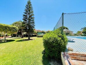 Ein eingezäunter Außenbereich mit Pool, einer großen Nadelbaum und einem gepflegten Rasen.